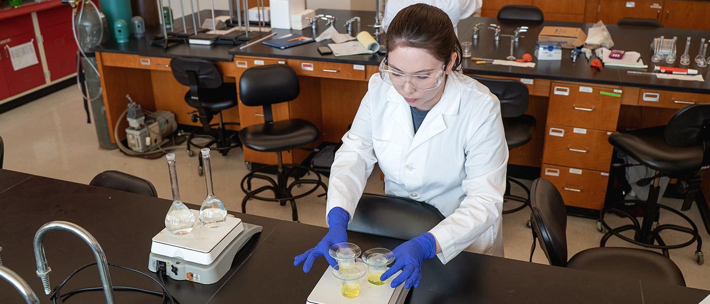 Chemistry student heating a yellow substance on a hot plate in a lab